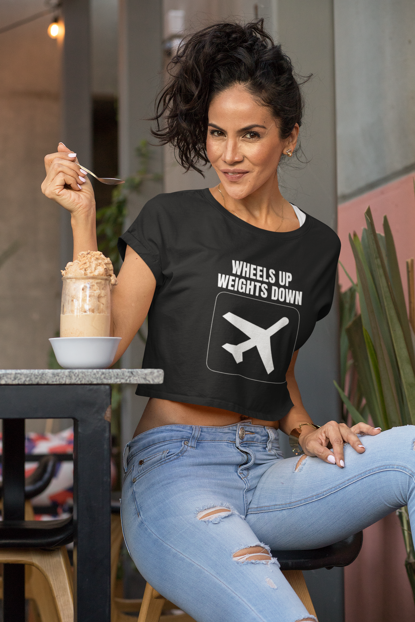 Woman road warrior wearing Wheels Up Weights Down black crop top holding a healthy smoothie post workout in luxury hotel gym