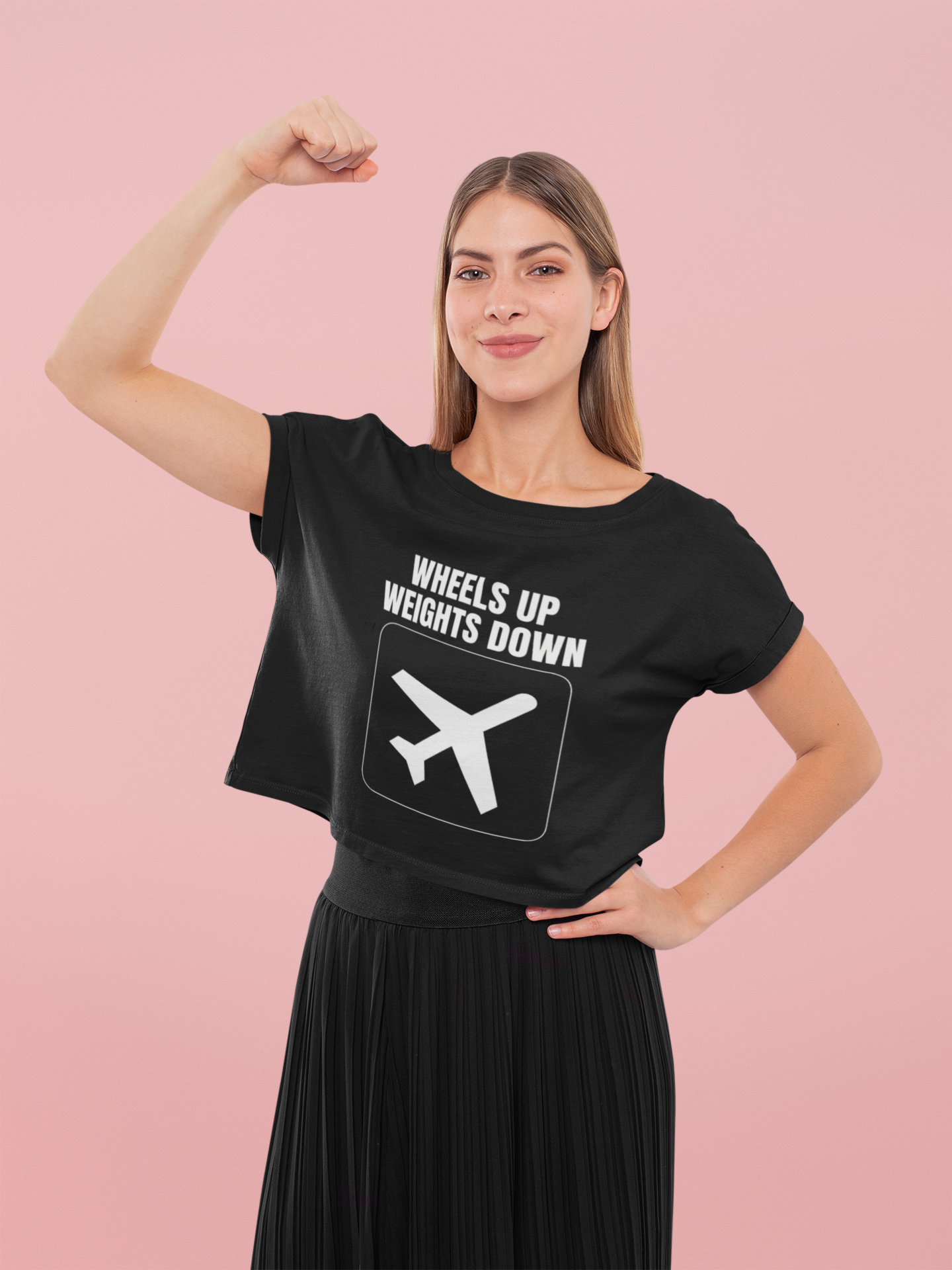 Female road warrior flexing strength in black Wheels Up Weights Down crop top travel fitness empowerment