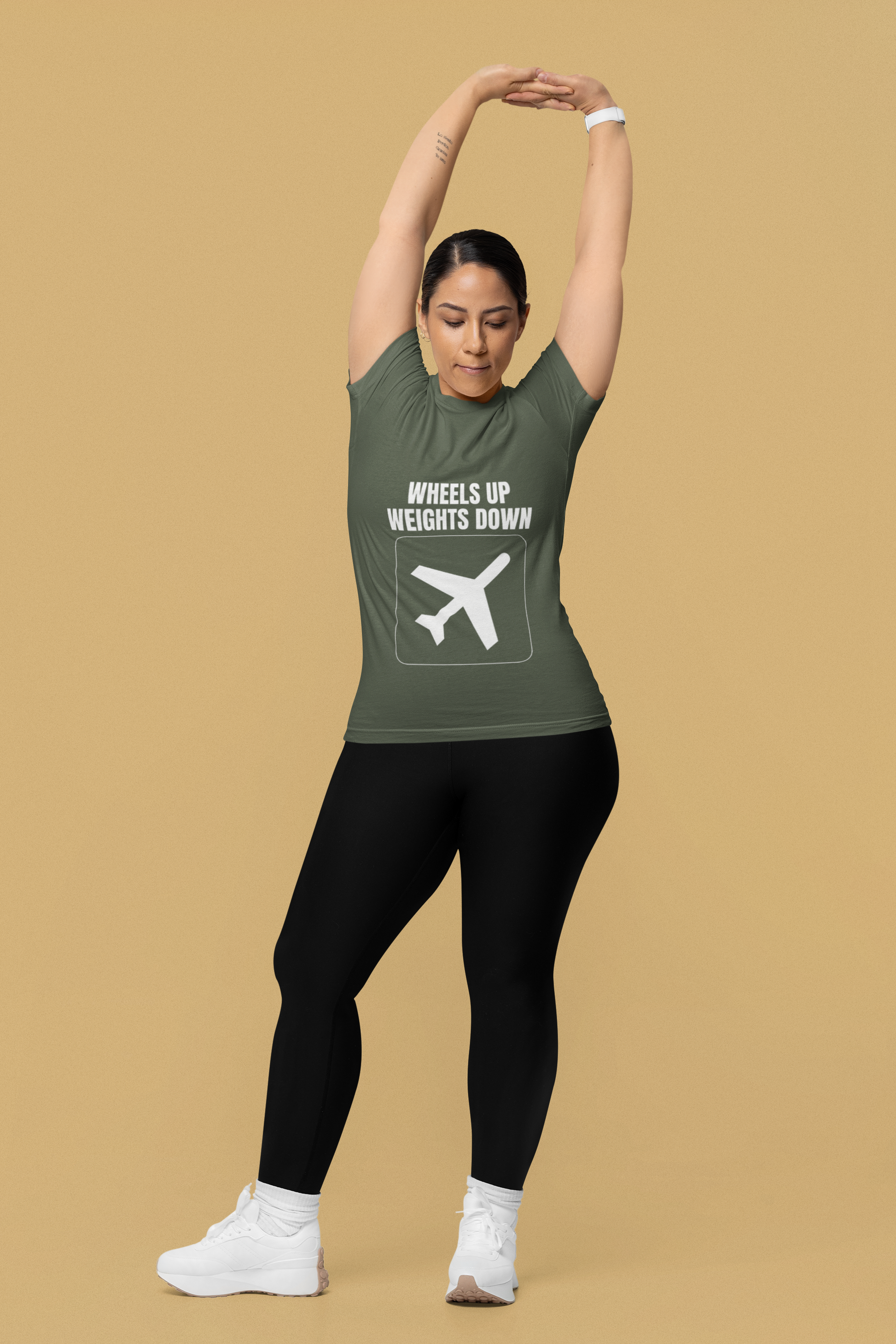 Woman stretching overhead in military green Wheels Up Weights Down travel gym t-shirt, travel nurse and corporate consultant fitness apparel