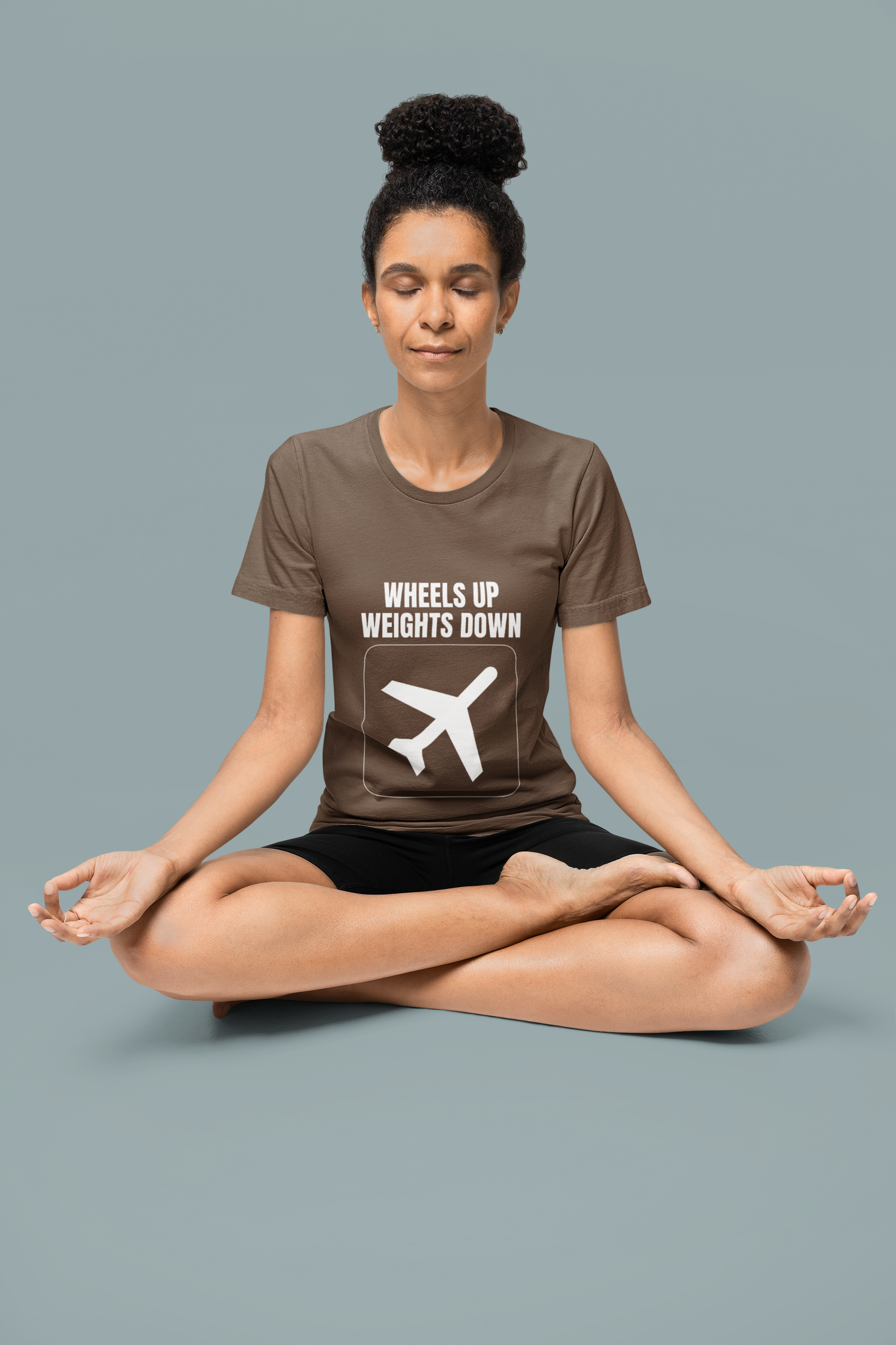 Woman in meditation pose wearing brown savana Wheels Up Weights Down travel gym t-shirt, veteran-founded premium travel fitness apparel